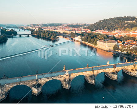 At sunrise, Charles Bridge stands majestically amidst the calm Vltava River, with the surrounding city of Prague glowing softly in the early light and promising a beautiful day ahead. 127965707