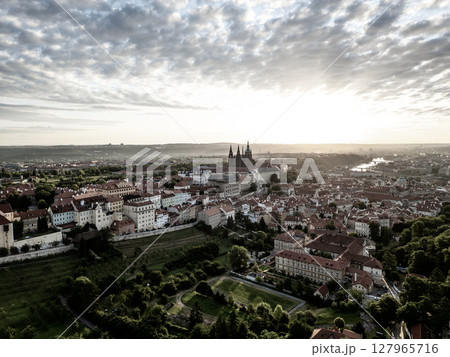 The sunrise casts a golden glow over Prague Castle and the surrounding city, showcasing the stunning architecture and serene atmosphere of early morning in Prague. 127965716
