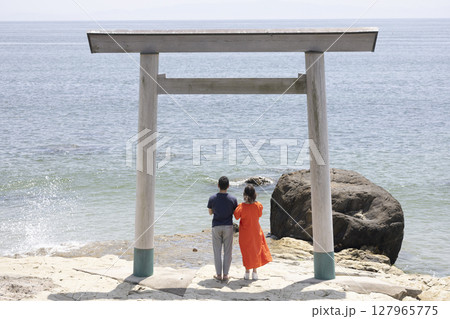 海岸沿いの鳥居の前に立つふたり 127965775