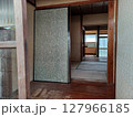 手前にガラス戸と傷んだ床、裏向きのふすま、奥に束ねられたケーブルが見える裏口からの古家の眺め 127966185