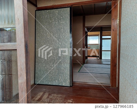 手前にガラス戸と傷んだ床、裏向きのふすま、奥に束ねられたケーブルが見える裏口からの古家の眺め 手前にガラス戸と傷んだ床、裏向きのふすま、奥に束ねられたケーブルが見える裏口からの古家の眺め 127966185