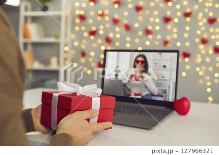 Close up of red gift box in male hands in front of laptop screen during online date. Close up of red gift box in male hands in front of laptop screen during online date. 127966321