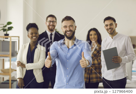 Smiling leader gesturing thumbs up standing with diverse business team in office 127966400