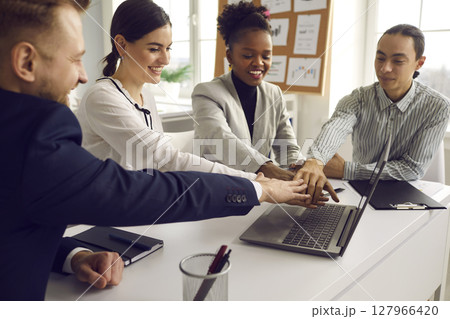 Multiracial diverse business team putting hand together sitting at office desk Multiracial diverse business team putting hand together sitting at office desk 127966420