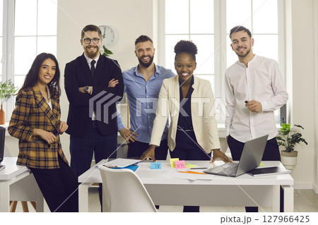 Team of happy young diverse business people standing in modern office and smiling Team of happy young diverse business people standing in modern office and smiling 127966425