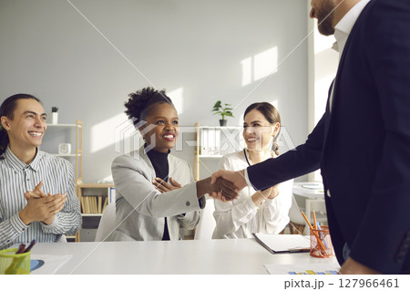 Happy woman smiling and shaking hands with her business partner in office meeting Happy woman smiling and shaking hands with her business partner in office meeting 127966461