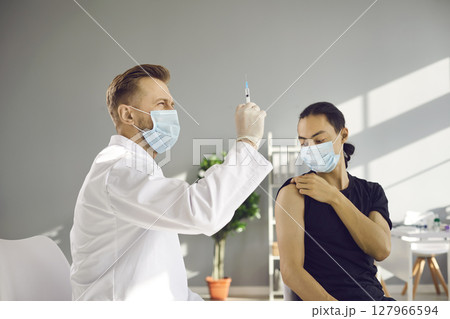 Doctor in medical face mask preparing syringe before giving injection to patient Doctor in medical face mask preparing syringe before giving injection to patient 127966594