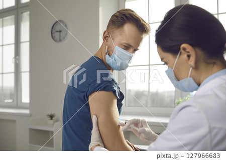 Young man in medical face mask getting vaccine injection during vaccination campaign 127966683