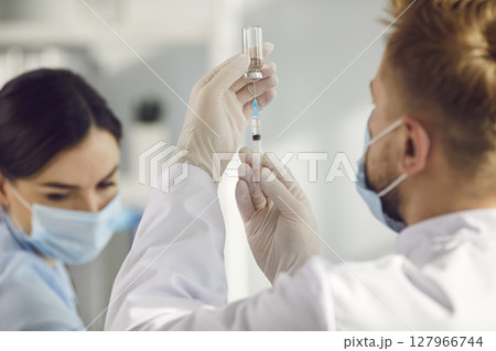 Doctor in uniform, mask and gloves filling syringe with vaccine before vaccination Doctor in uniform, mask and gloves filling syringe with vaccine before vaccination 127966744
