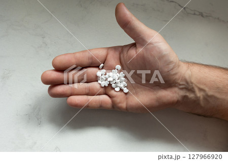 Hand Holding White Pills on a Smooth Surface at a Home or Clinic Setting 127966920