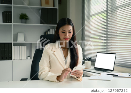 Elegant businesswoman in beige suit using mobile phone at clean white desk Elegant businesswoman in beige suit using mobile phone at clean white desk 127967252