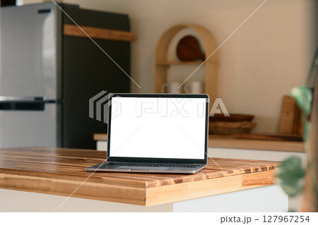 Laptop on a clean countertop with a refrigerator and kitchen decor in the background 127967254