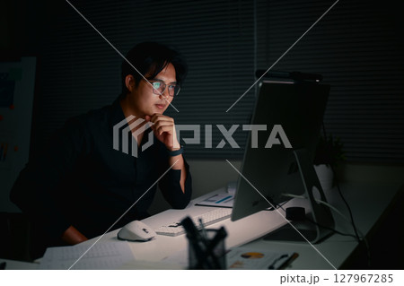 Focused businessman staying late to complete important projects,in a dimly lit office. 127967285