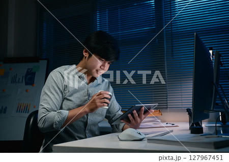 Focused office worker reviewing documents while working late into the night 127967451