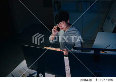 Office worker working late into the evening reading paperwork and phone communication at desk 127967460