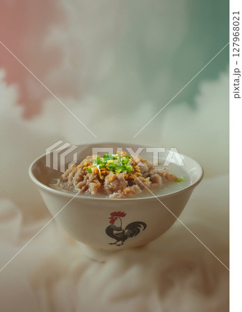 Hearty bowl of Asian pork gruel or congee, topped with fresh scallions and crunchy fried garlic, presented in a rustic ceramic bowl. Hearty bowl of Asian pork gruel or congee, topped with fresh scallions and crunchy fried garlic, presented in a rustic ceramic bowl. 127968021