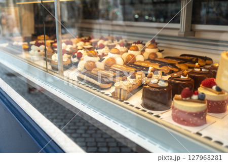 Glass display of a French patisserie showcasing various gourmet pastries including eclairs, tarts 127968281