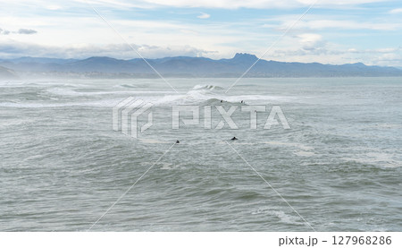 Surfers in wetsuits wait for waves in the cold Atlantic Ocean near Biarritz, France 127968286