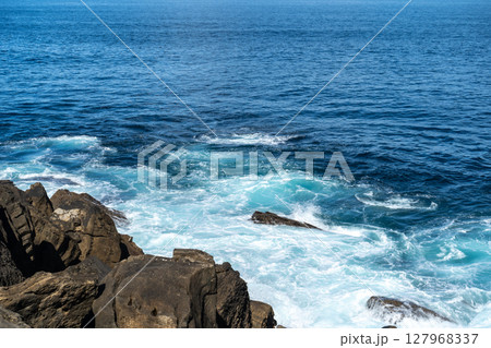 Wave impact exposes basalt layers and erosion patterns 127968337