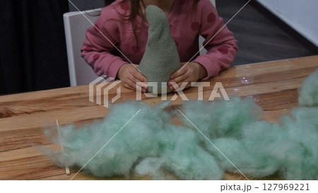 Kid girl hands stuffing handcrafted felt toy using green sintepon cotton filling 127969221