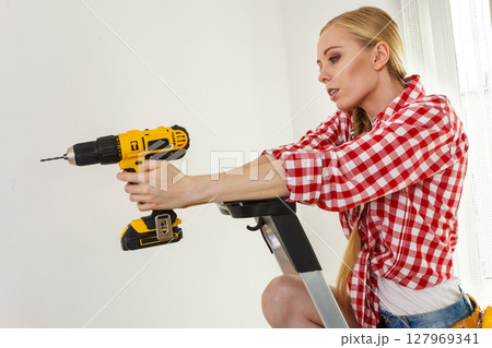 Woman using drill on ladder Woman using drill on ladder 127969341