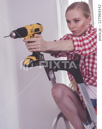 Woman using drill on ladder Woman using drill on ladder 127969342