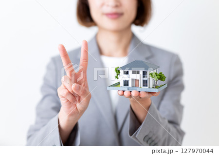 家の住宅模型を持って2本指を立てるグレーのスーツ姿のミドル女性 家の住宅模型を持って2本指を立てるグレーのスーツ姿のミドル女性 127970044