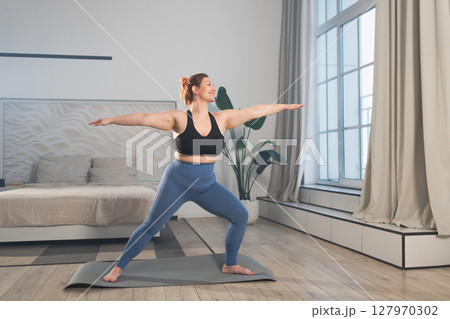 Yoga fitness workout training. Woman practicing yoga at home. Plus size female doing sports exercise on yoga mat indoor. Girl in sportswear have training workout for weight loss. Sport and fitness Yoga fitness workout training. Woman practicing yoga at home. Plus size female doing sports exercise on yoga mat indoor. Girl in sportswear have training workout for weight loss. Sport and fitness 127970302