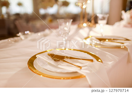 table decoration with pink tablecloth, crystal candlesticks with candles and white pink flowers in restaurant . stylish wedding day. setting table with gold plate, fork and knife 127970714