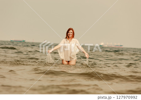 Redhead woman playing in water during summertime 127970992