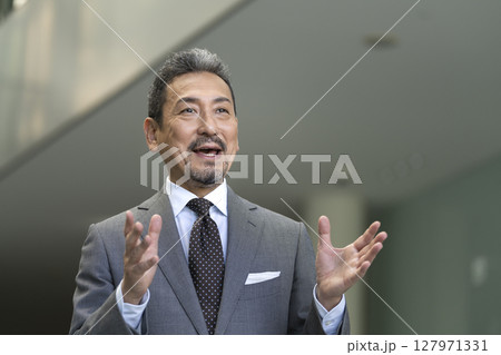 身振りを交えて話すスーツ姿のシニア男性 身振りを交えて話すスーツ姿のシニア男性 127971331