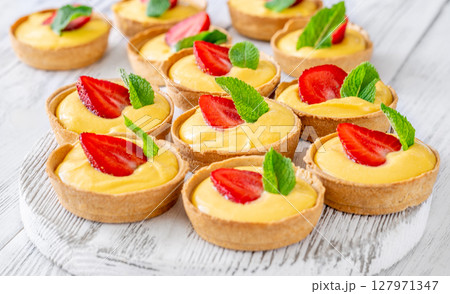 Mini mango cream tarts with strawberry and mint on white wooden board Mini mango cream tarts with strawberry and mint on white wooden board 127971347
