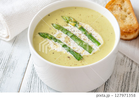 Creamy asparagus soup in white bowl with swirl and toasted ciabatta 127971358
