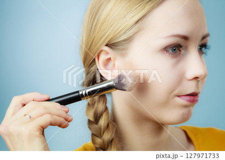 Makeup artist applying with brush rouge on female check Makeup artist applying with brush rouge on female check 127971733
