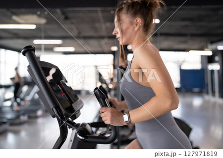 Woman training and fitness in gym on elliptical machine for health, wellness and cardio endurance. Cyclist, exercise bike and performance on equipment, power challenge and intense workout 127971819
