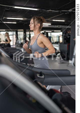 Side view of beautiful muscular woman running on treadmill. Side view of beautiful muscular woman running on treadmill. 127971833