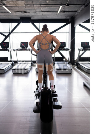 A woman is actively exercising on an elliptical machine at a modern gym facility 127971839