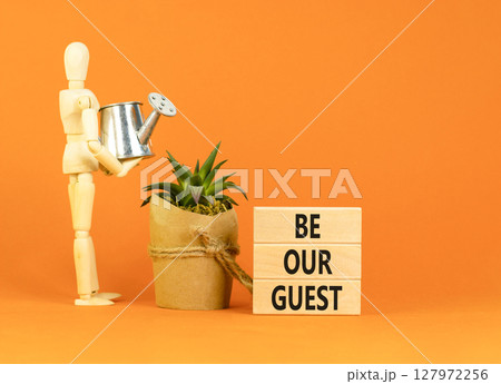Be our guest symbol. Concept words Be our guest on beautiful wooden block. Businessman model. Beautiful orange background. Business and be our guest concept. Copy space. Be our guest symbol. Concept words Be our guest on beautiful wooden block. Businessman model. Beautiful orange background. Business and be our guest concept. Copy space. 127972256