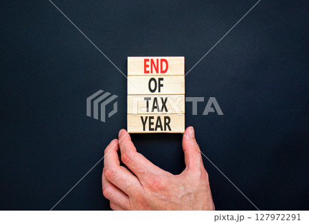 End of tax year symbol. Concept words phrase End of tax year on beautiful wooden blocks. Beautiful black paper background. Businessman's hand. Business End of tax year concept. Copy space. End of tax year symbol. Concept words phrase End of tax year on beautiful wooden blocks. Beautiful black paper background. Businessman's hand. Business End of tax year concept. Copy space. 127972291