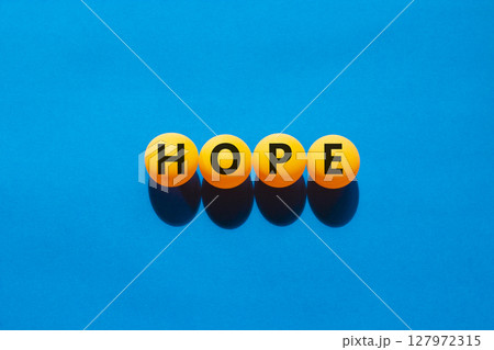 Hope symbol. Concept word Hope on beautiful yellow ping pong balls. Beautiful blue table blue background. Business, lifestyle, support and hope concept. Copy space. Hope symbol. Concept word Hope on beautiful yellow ping pong balls. Beautiful blue table blue background. Business, lifestyle, support and hope concept. Copy space. 127972315