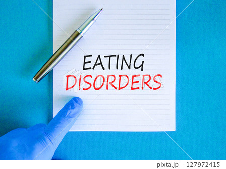 Eating disorders symbol. Concept words Eating disorders on beautiful white note. Doctor's hand in blue medical glove. Beautiful blue background. Medical healthy lifestyle eating disorders concept. Eating disorders symbol. Concept words Eating disorders on beautiful white note. Doctor's hand in blue medical glove. Beautiful blue background. Medical healthy lifestyle eating disorders concept. 127972415