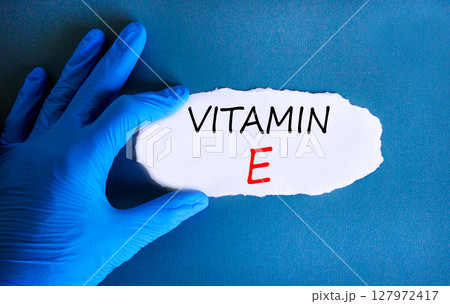 Vitamin E tocopherols symbol. Concept words Vitamin E on beautiful white paper. Doctor's hand in blue medical glove. Beautiful blue background. Medical healthy lifestyle Vitamin E tocopherols concept. Vitamin E tocopherols symbol. Concept words Vitamin E on beautiful white paper. Doctor's hand in blue medical glove. Beautiful blue background. Medical healthy lifestyle Vitamin E tocopherols concept. 127972417