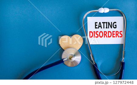 Eating disorders symbol. Concept words Eating disorders on beautiful white card. Wooden heart and stethoscope. Beautiful blue background. Medical healthy lifestyle eating disorders concept. Eating disorders symbol. Concept words Eating disorders on beautiful white card. Wooden heart and stethoscope. Beautiful blue background. Medical healthy lifestyle eating disorders concept. 127972448