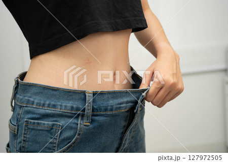 Young Asian woman losing weight wearing loose pants in oversize jeans. Young Asian woman losing weight wearing loose pants in oversize jeans. 127972505