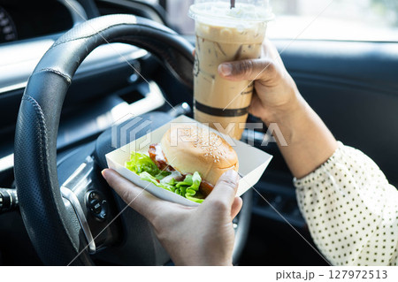 Asian woman driver hold and eat hamburger in car, dangerous and risk an accident. Asian woman driver hold and eat hamburger in car, dangerous and risk an accident. 127972513