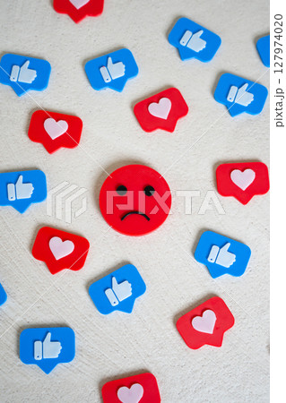 Sad face surrounded by likes and hearts from social networks. Chasing likes does not make you happy. Internet addiction, doomscrolling. Endorphin addiction. Emotional burnout in digital culture 127974020