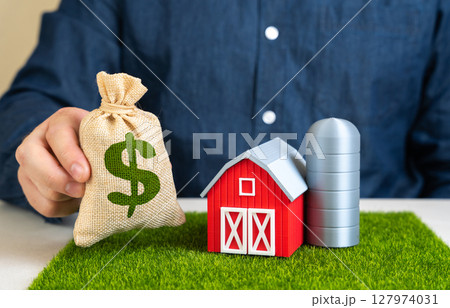 Man holding dollar money bag near farm. Buying or selling a farm. High demand for starting your own business in the countryside. Farming trend. Subsidies, farm acquisition. Rural entrepreneurship 127974031