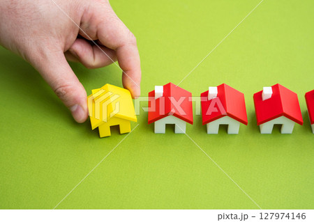 The hand places the yellow house in a row with the others. A unique offer. Milestone achieved through the sale or construction of real estate. Project completion. Importance of choosing the right home The hand places the yellow house in a row with the others. A unique offer. Milestone achieved through the sale or construction of real estate. Project completion. Importance of choosing the right home 127974146