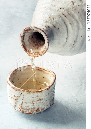 Sake poured into ochoko, traditional cup, on a slate background, a close-up Sake poured into ochoko, traditional cup, on a slate background, a close-up 127974651