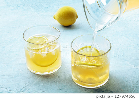 Lemonade poured from a jug into a glass, with a fresh lemon Lemonade poured from a jug into a glass, with a fresh lemon 127974656